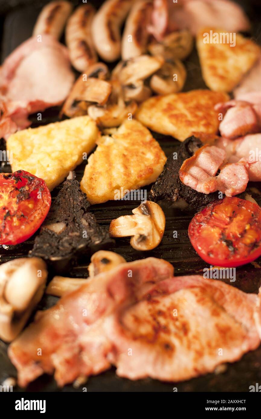 Close up view of grilled tomato and mushroom cooking besides four sausage links and other meats Stock Photo