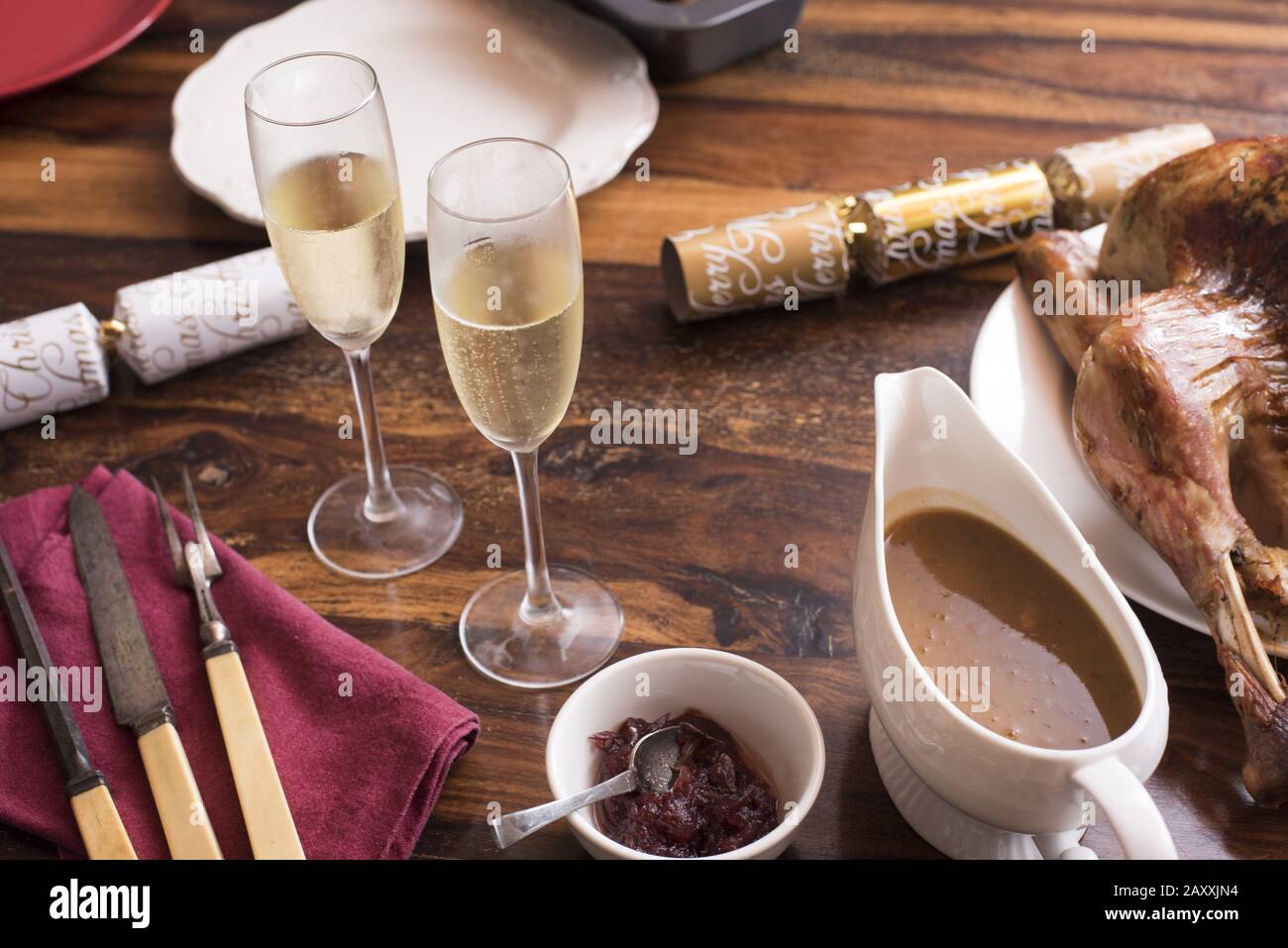 Christmas dinner still life with champagne, roast turkey, gravy, cranberry sauce, crackers and carving utensils on a wooden table Stock Photo