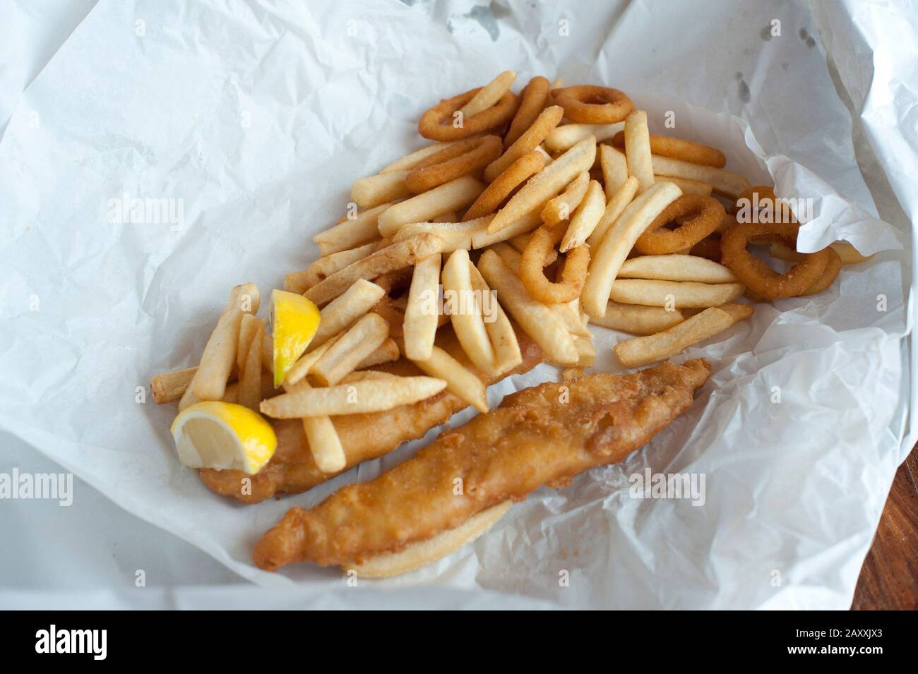 Overhead view of fried fish fillets in batter, calamari rings and potato chips on crumpled paper Stock Photo