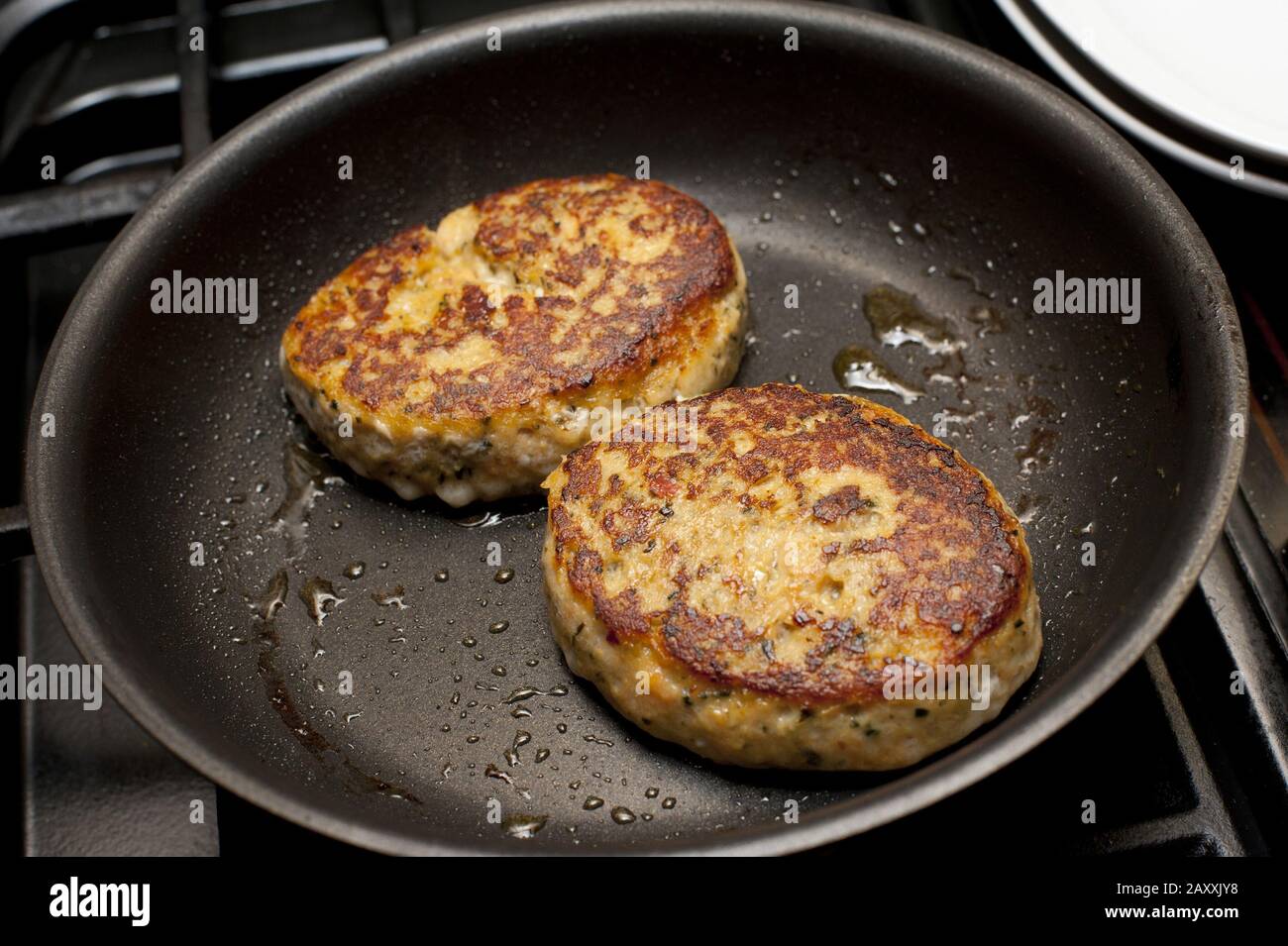 Close up on two round well cooked fried fish patties in non-stick pan with light coating of oil Stock Photo