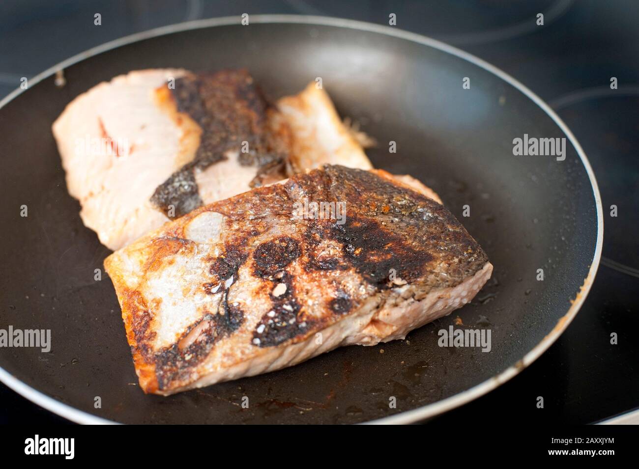 Searing salmon fish fillet steaks in a pan over the stove while pan-frying a delicious healthy seafood dinner Stock Photo