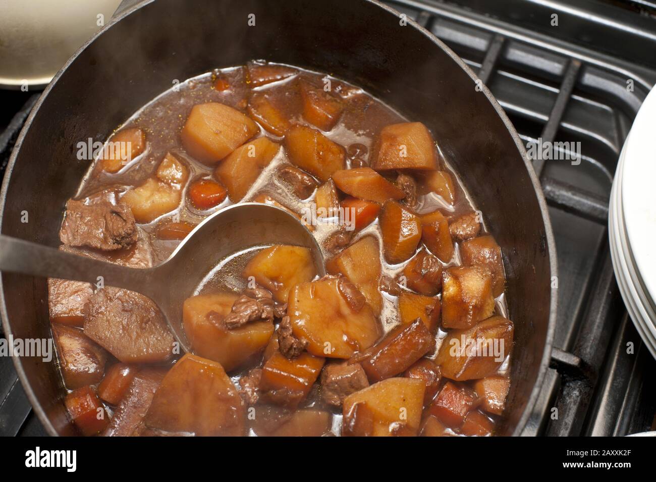 Delicious hot soup or stew with potatoes, meat, different vegetables in saucepan on stove. From above Stock Photo