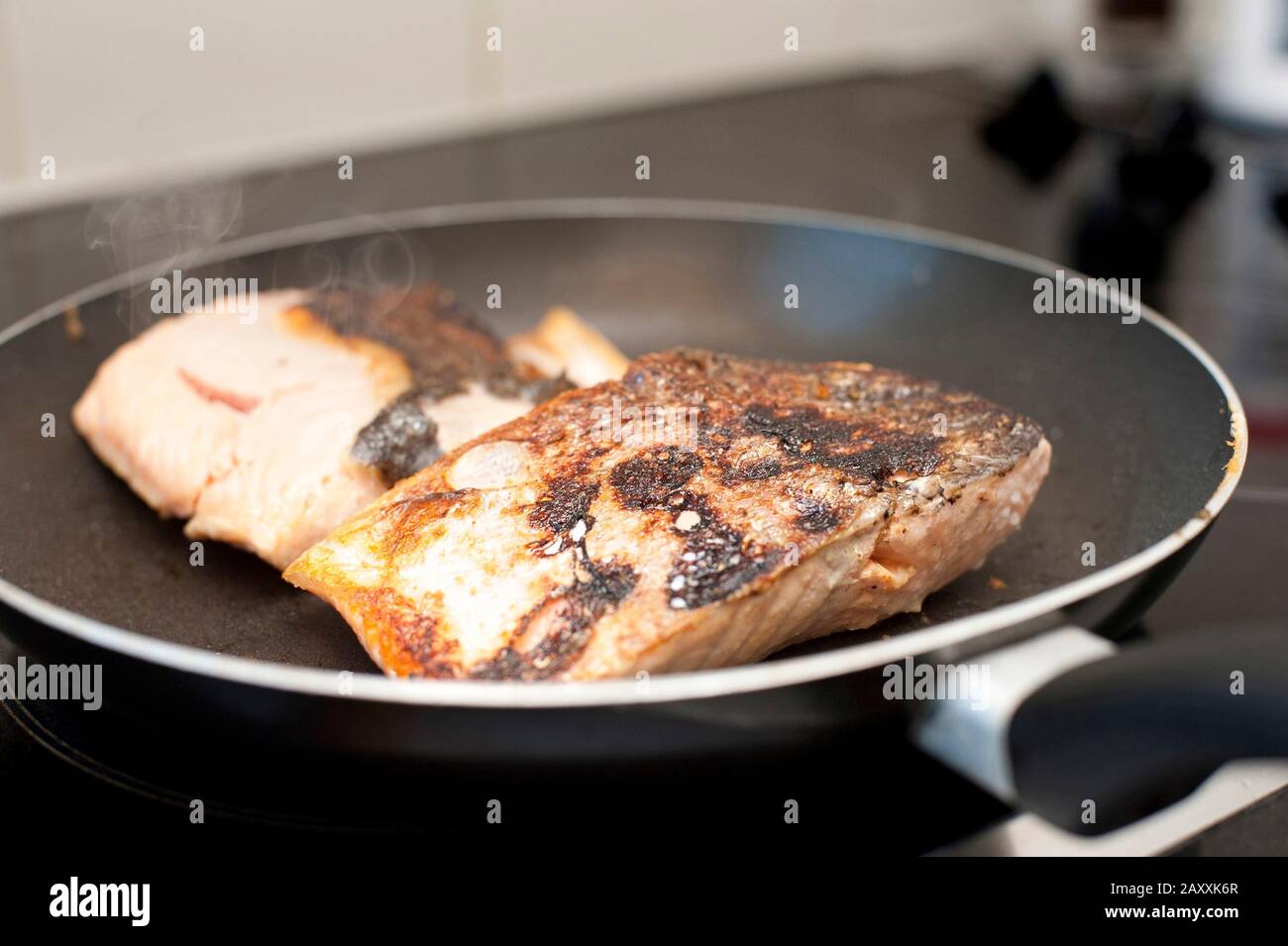 Fresh salmon steaks searing in the hot pan while preparing a healthy seafood dinner over the stove Stock Photo