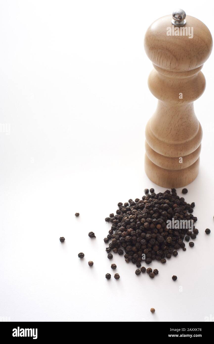 Wooden pepper mill or grinder with a heap of dried black peppercorns