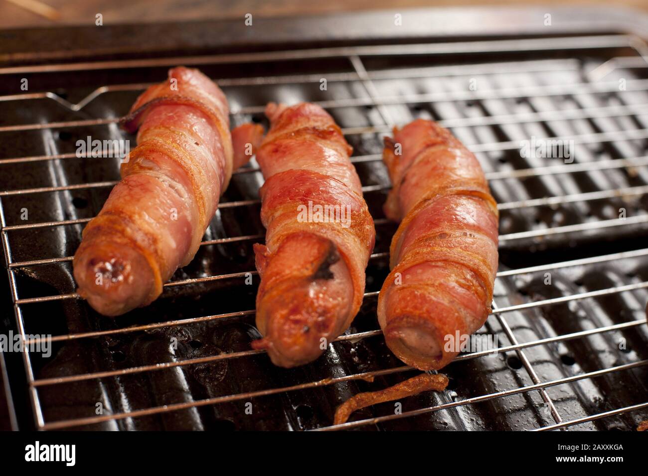 Pork sausage and bacon rolls, or traditional pigs in blankets, on a grill in close up Stock Photo