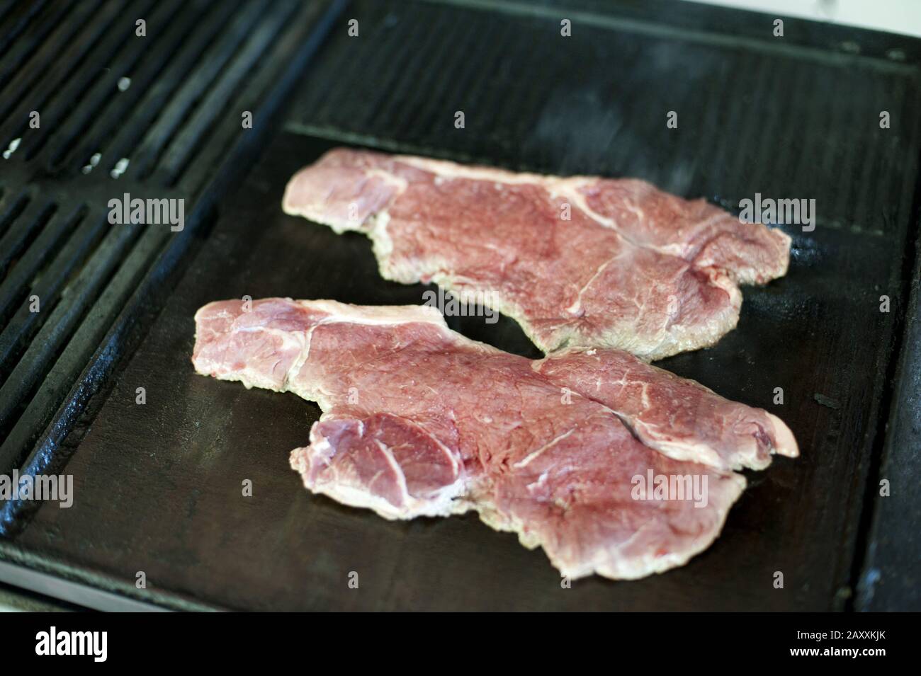 Two lean tender strip steaks cooking over a BBQ griddle viewed high