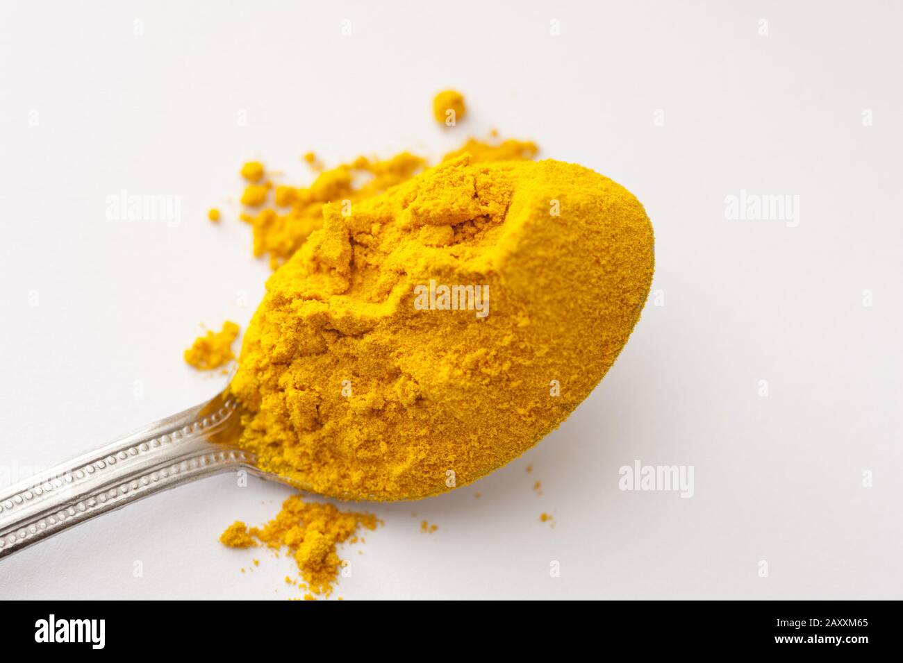 Silver teaspoon heaped with ground dried turmeric powder over a white background with copy space Stock Photo