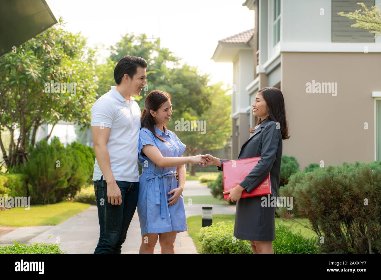 Happy Asian couple looking for their new house and shake hands with real estate broker after a deal. Young couple handshaking real estate agent after Stock Photo