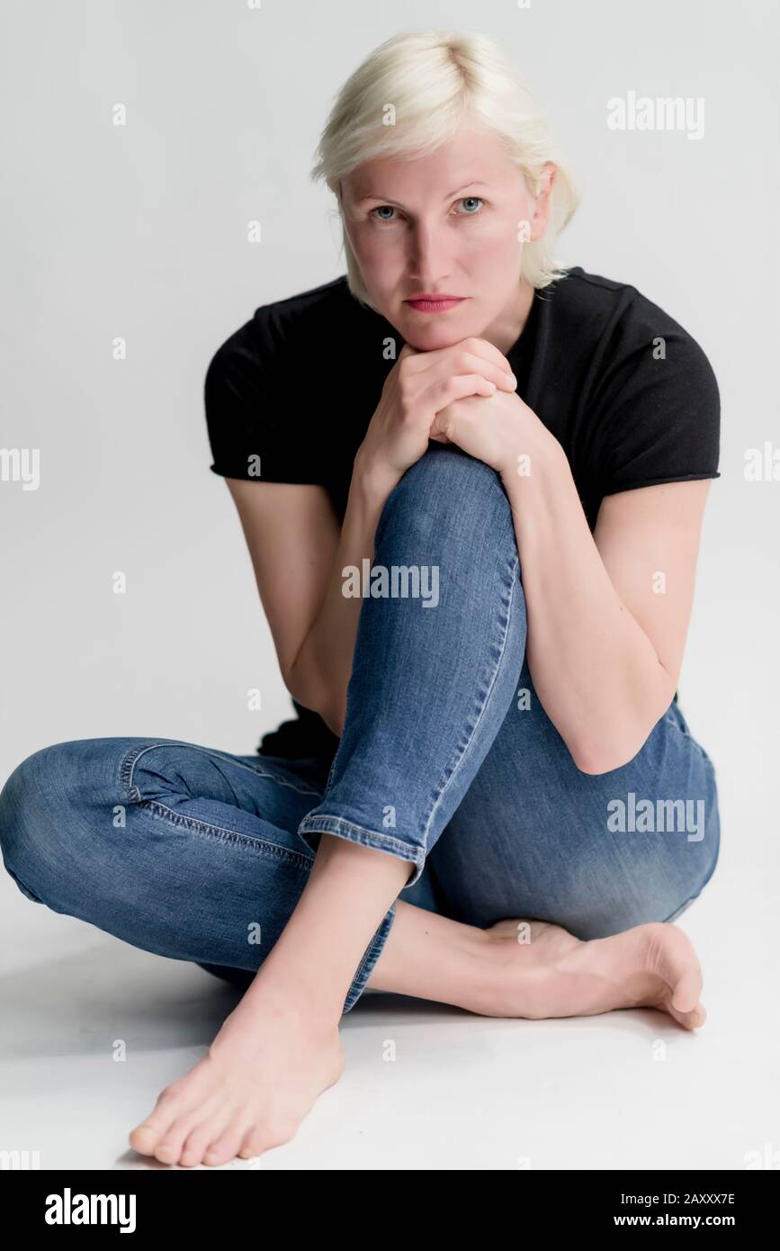 Portrait of attractive young blond woman sitting on floor and looking ...
