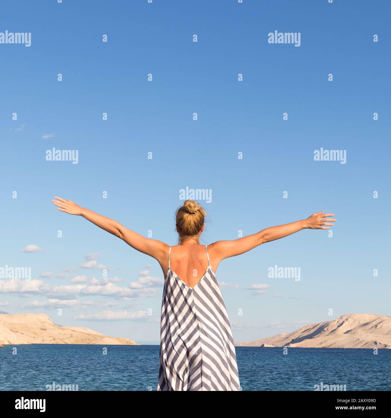 Happy carefree woman rising arms, wearing beautiful striped summer dress  enjoying late afternoon on white pabbled beach on Pag island, Croatia Stock  Photo - Alamy