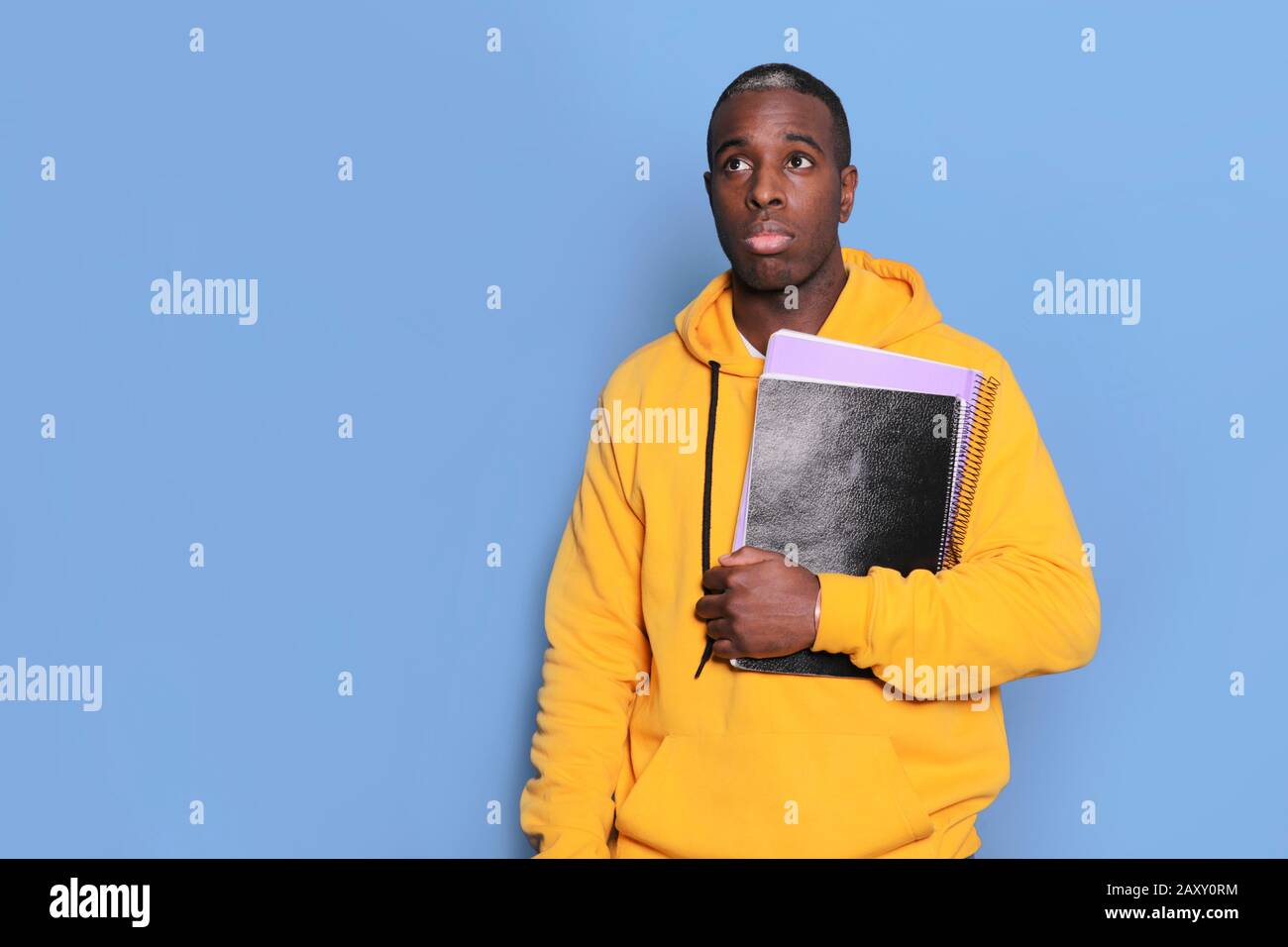 Confused black young man has hesitant expression, holds textbook, isolated over blue background Stock Photo