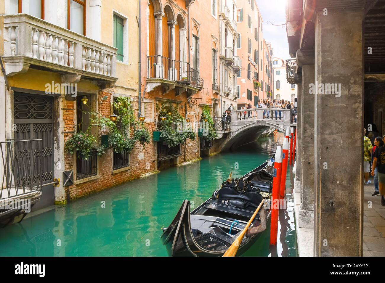 Tourists cross a bridge over a small canal with a gondola parked in the historic center of Venice Italy. Stock Photo