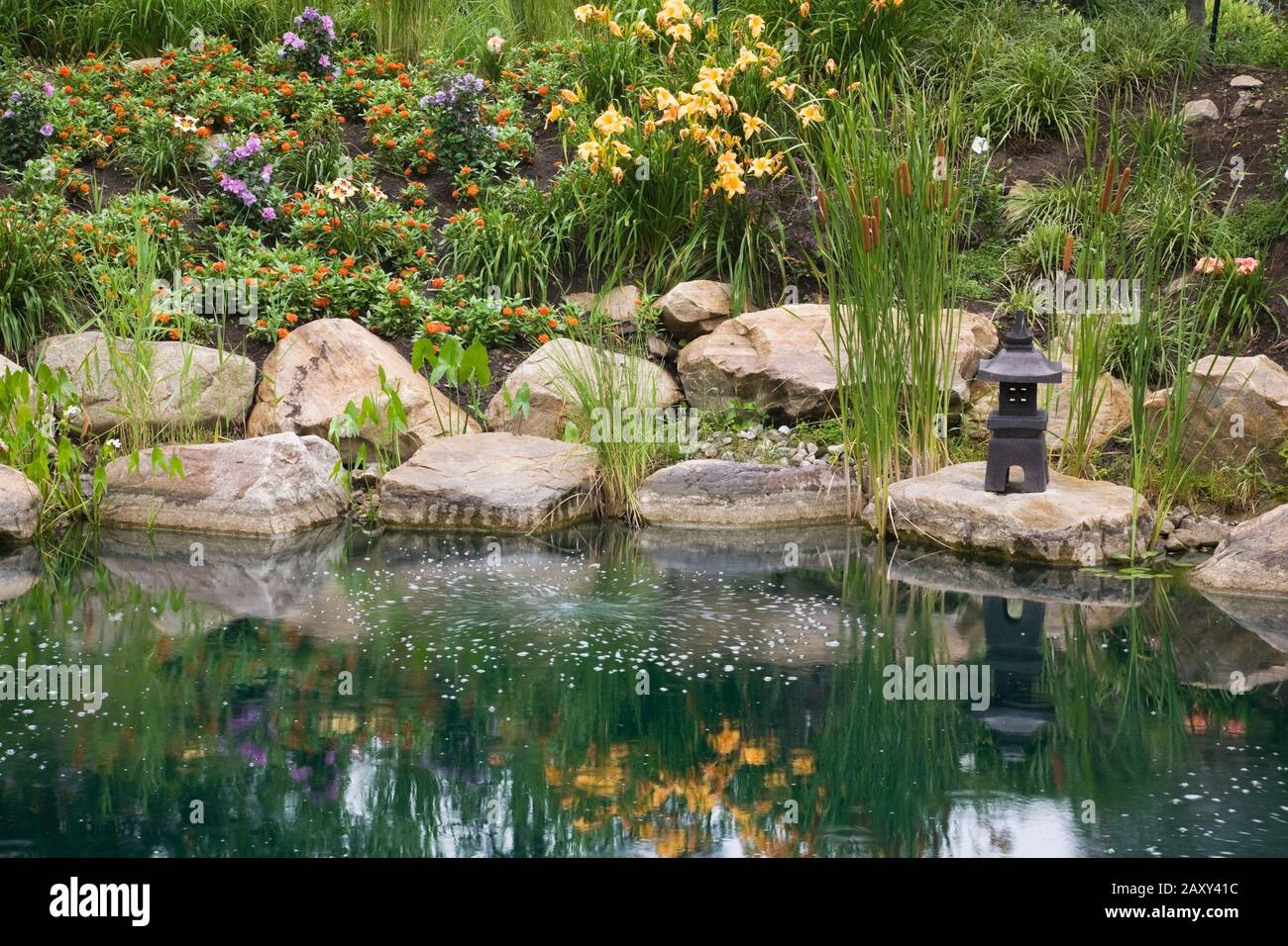 Pond with pagoda sculpture, Typha latifolia - Common Cattails, Pondeteria cordata - Pickerel Weed plants bordered by orange Hemerocallis - Daylilies. Stock Photo