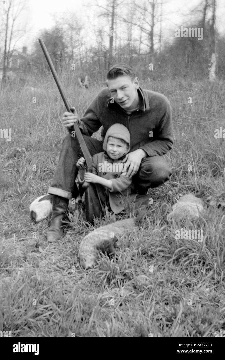 A father and son pose with their firearm while hunting, ca. 1950. Stock Photo