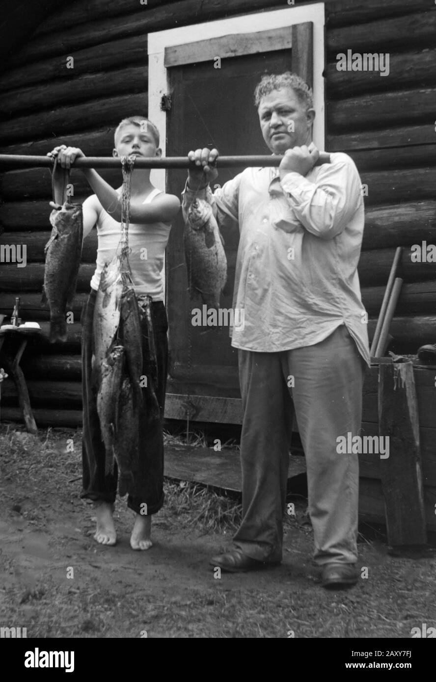 Father and son display their catch after a day of fishing at their cabin, ca. 1960. Stock Photo