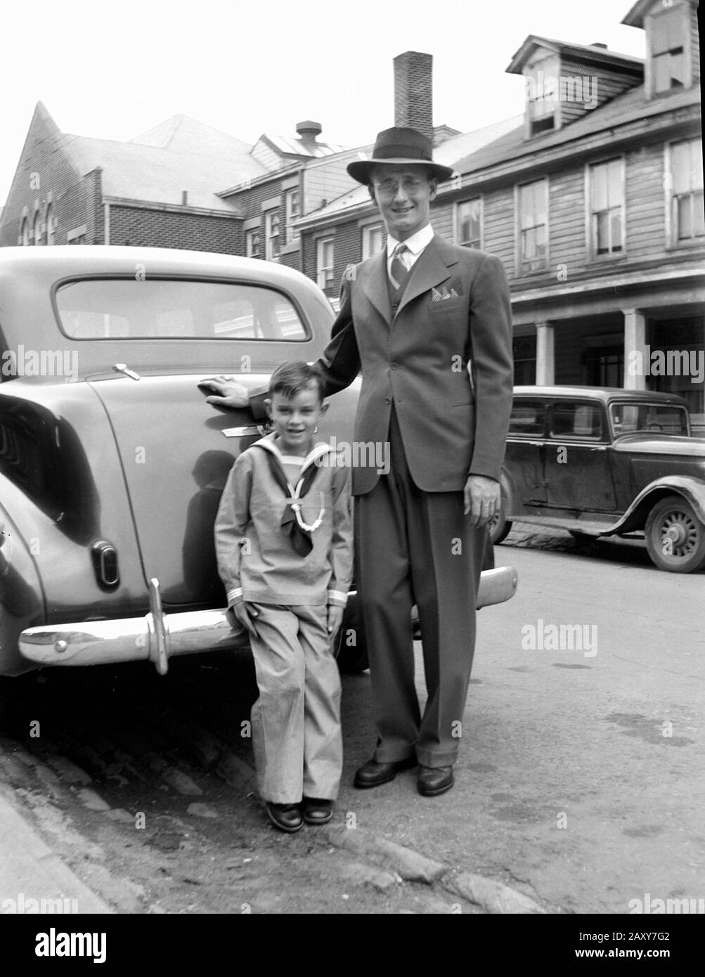 Father and son pose by the bumper of their family car, ca. 1935. Stock Photo