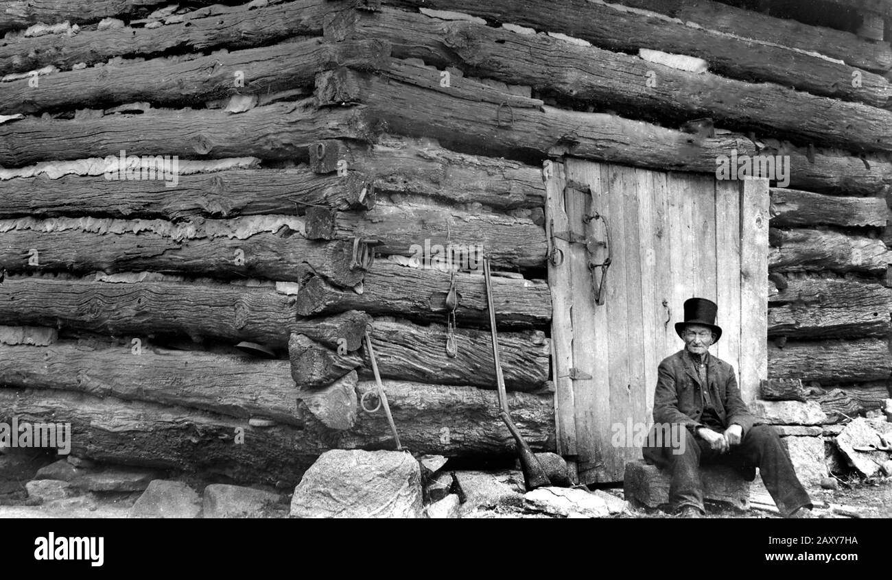 A senior man sits outside his log cabin, ca. 1900. Stock Photo