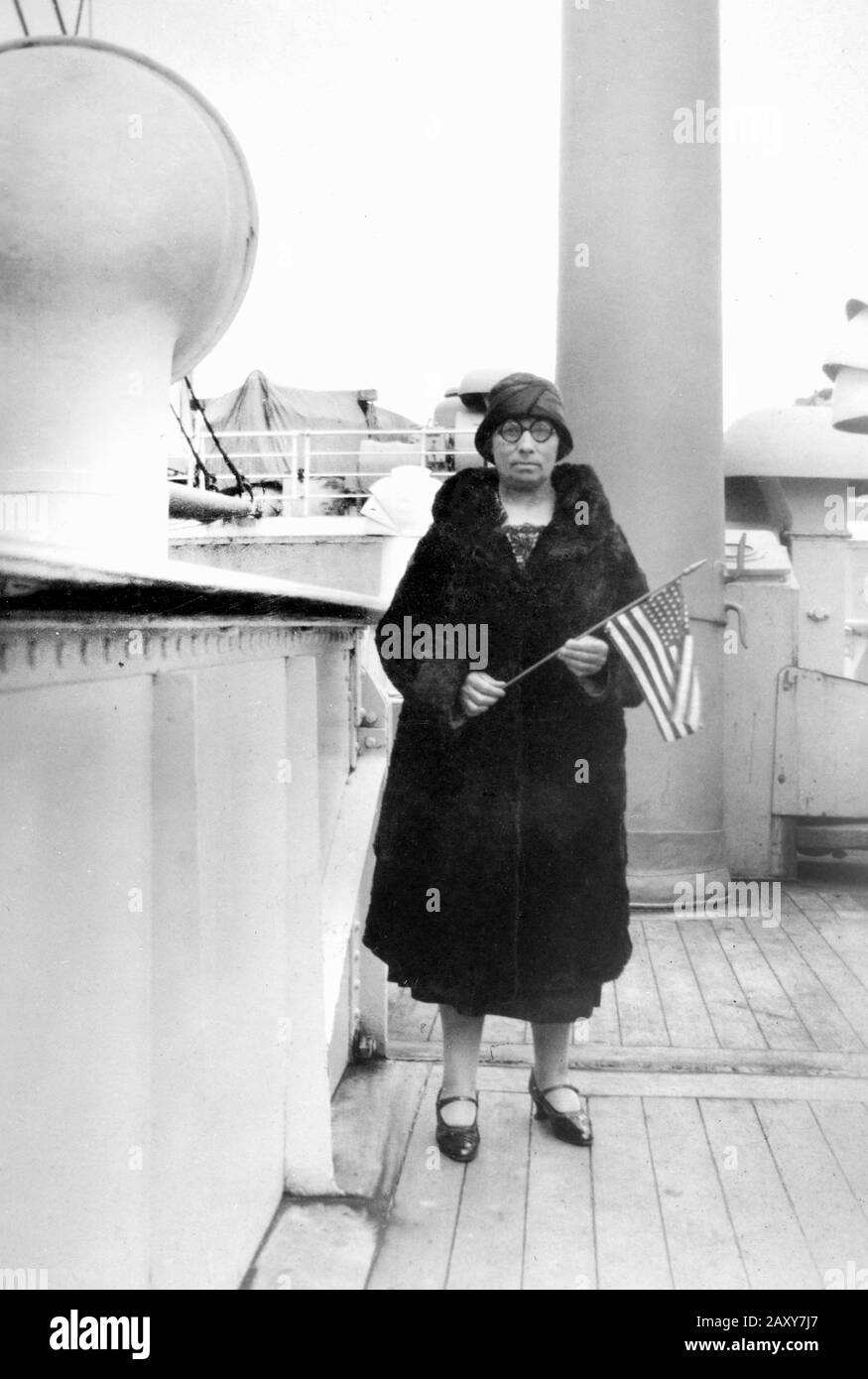 A iwoman on a ship deck stands with an American flag, ca. 1910. Stock Photo