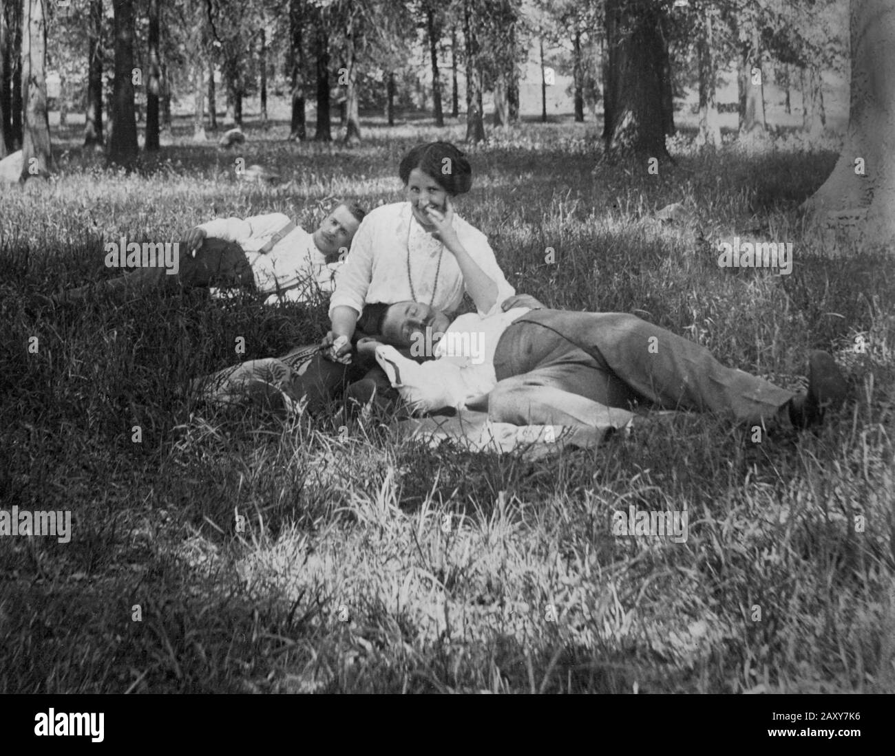 A woman has a sly smile while one man sleeps it off and another lurks in the background, ca. 1910. Stock Photo