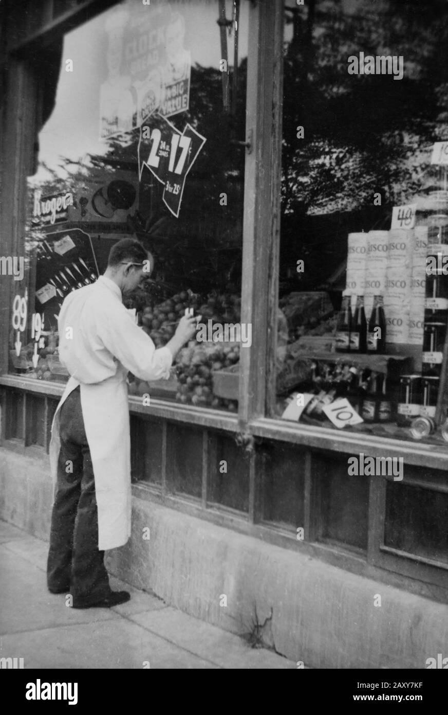 A grocer in a Chicago Kroger store paints a price display on his store window, ca. 1940. Stock Photo