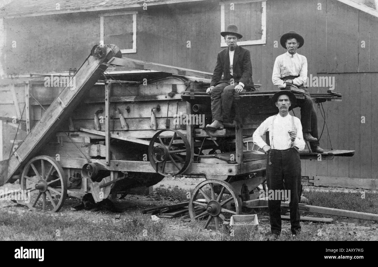 Three farmers take a break from working on an early combine on the American plains for portrait, 1910. Stock Photo