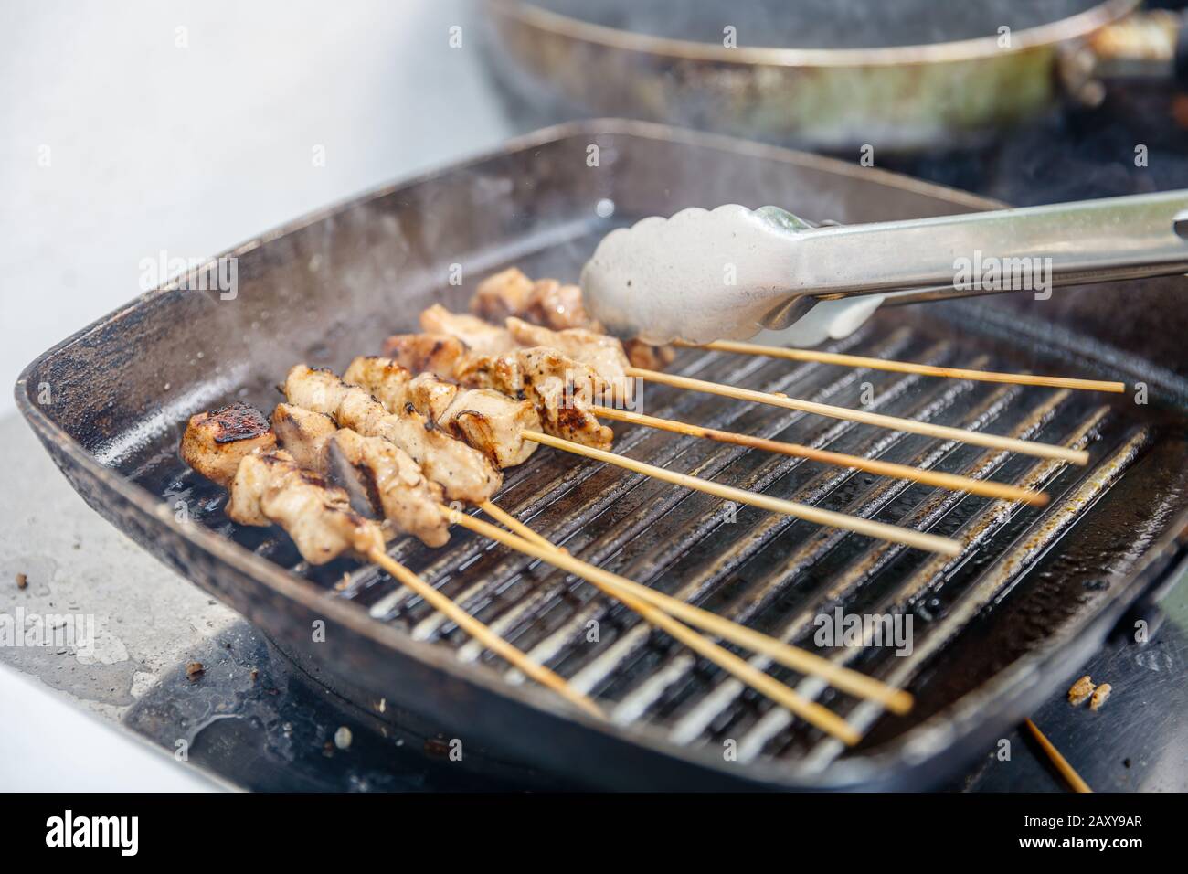 Sate ayam - grilled chicken meat on wooden skewers cooked on a cast fry pan. Indonesian cuisine. Stock Photo