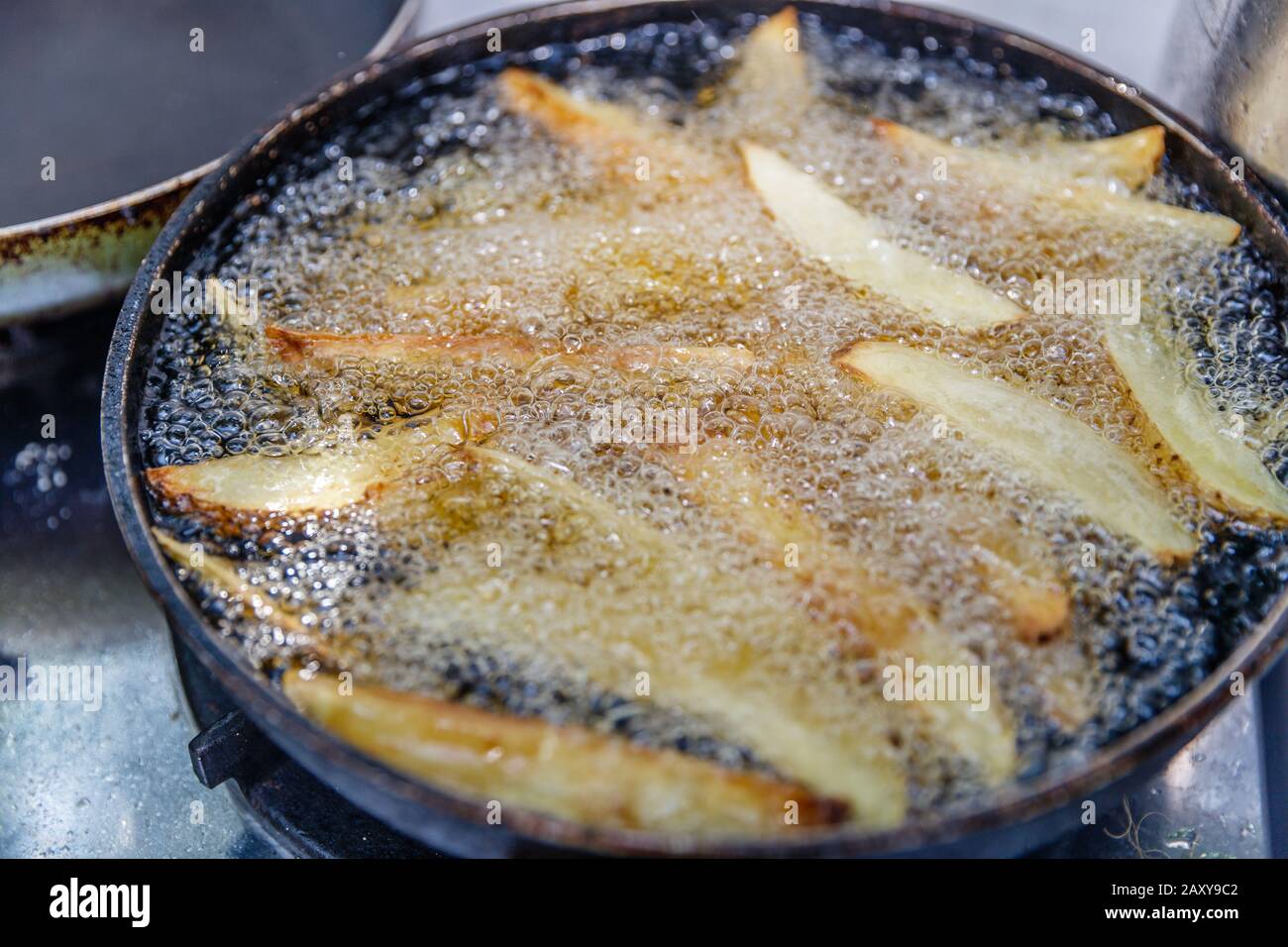 Seasoned potato wedges frying in hot oil on a cast iron fry pan