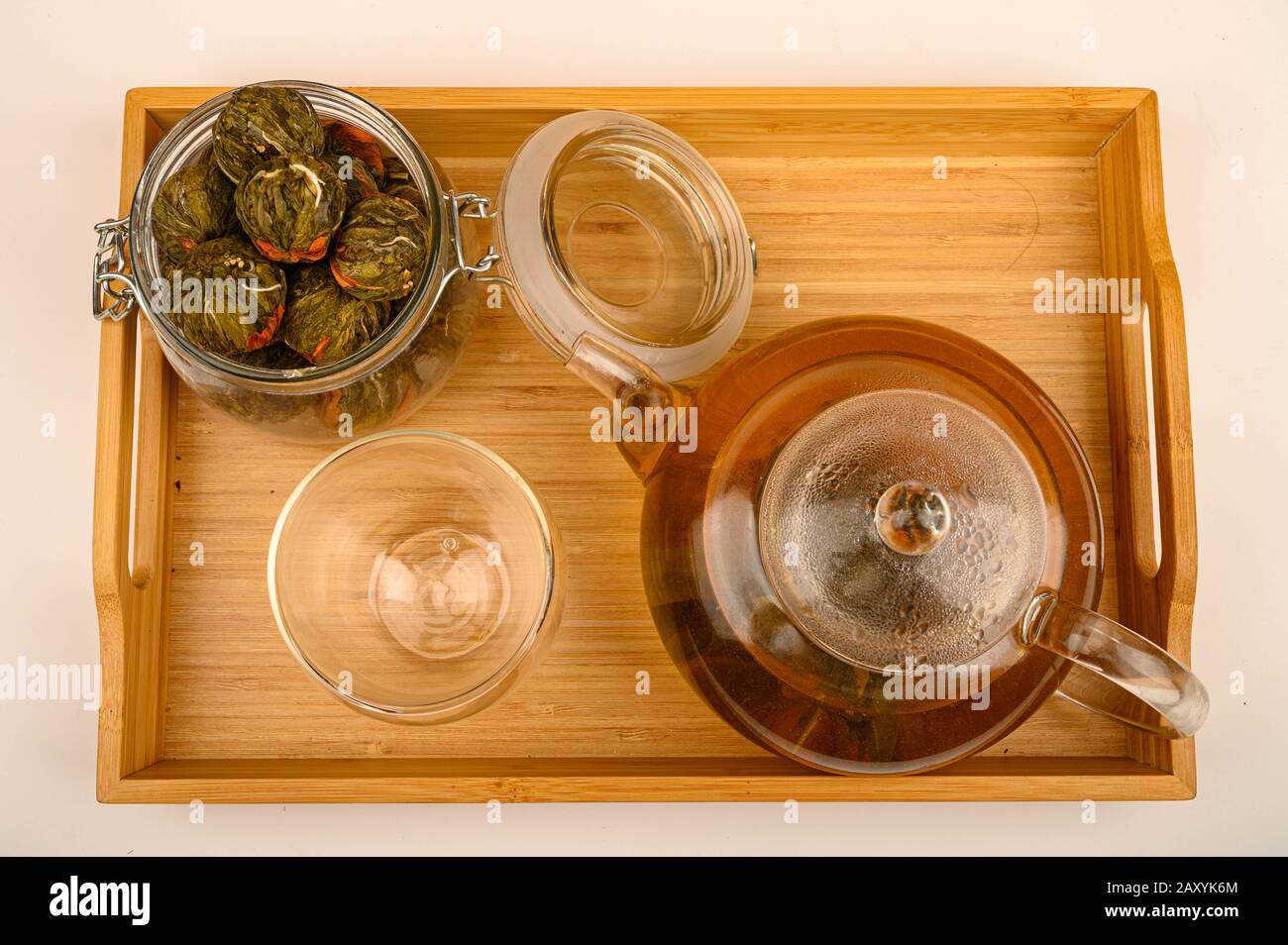 Flower tea brewed in a glass teapot, glass and jar with flower tea balls on a wooden tray on a white background. Close up Stock Photo
