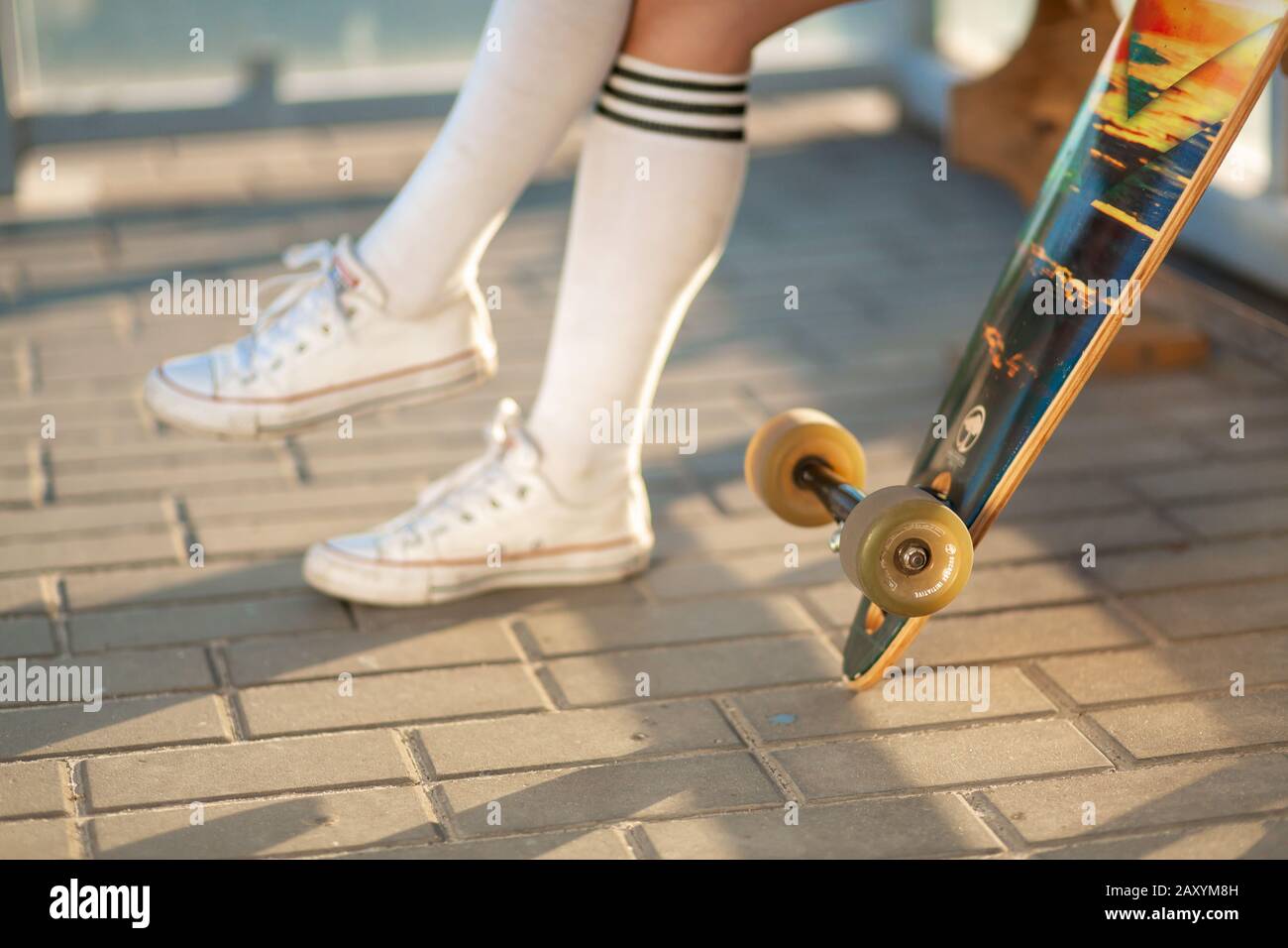 Stylish young girl sitting on bus stop with her longboard, drink soda and wait for bus Stock