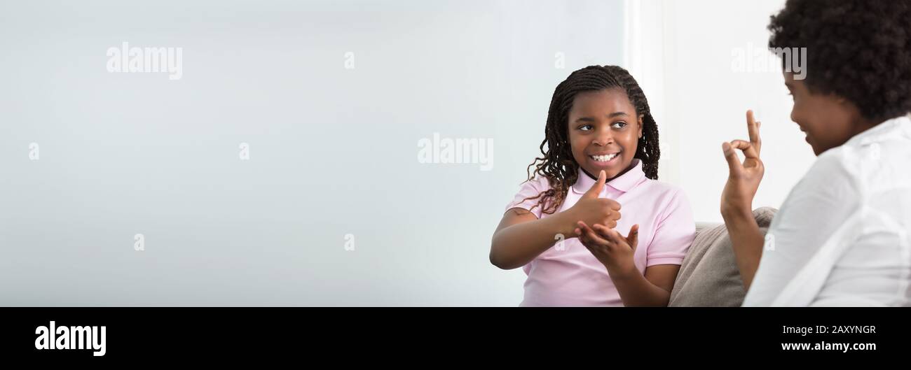 Mother Learning Sign Language To Talk With Her Hearing Impairment Daughter Stock Photo