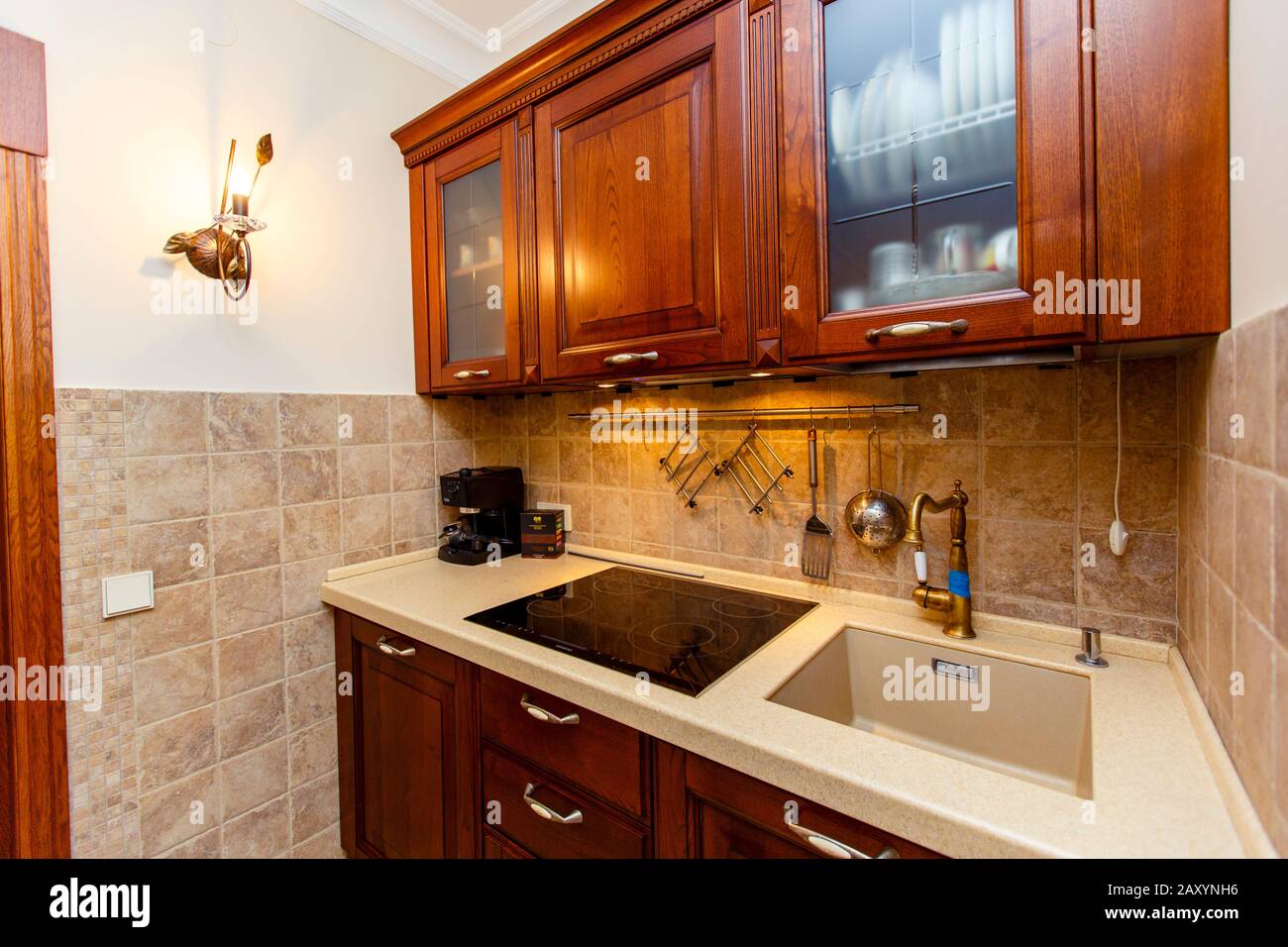 A small kitchen in the cottage. Sink and electric stove. Above the shelf and a set of dishes.. Stock Photo