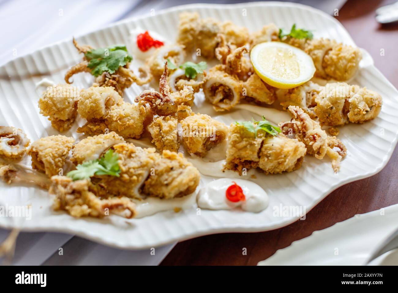 Deepfried battered cut calamari with tartar sauce and lemon. served on a white ceramic plate