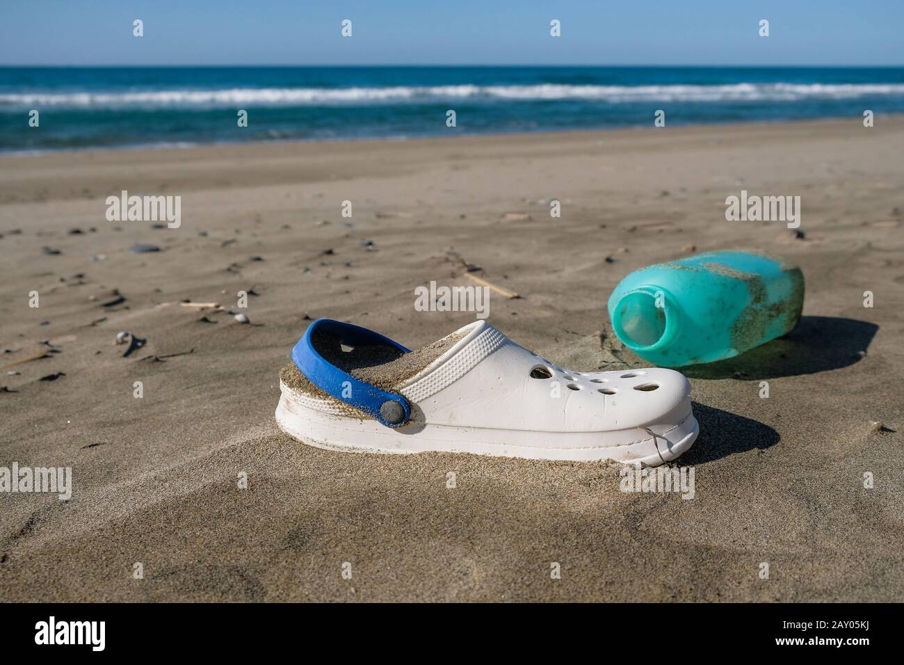 Summer slippers and plastic container on wild polluted sea coast ecosystem,italy Stock Photo