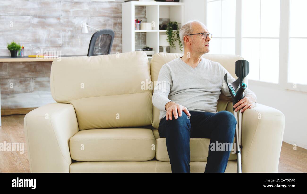 Revealing shot of male nurse checking on retired old man with alzheimer sitting on a couch in the nursing home Stock Photo