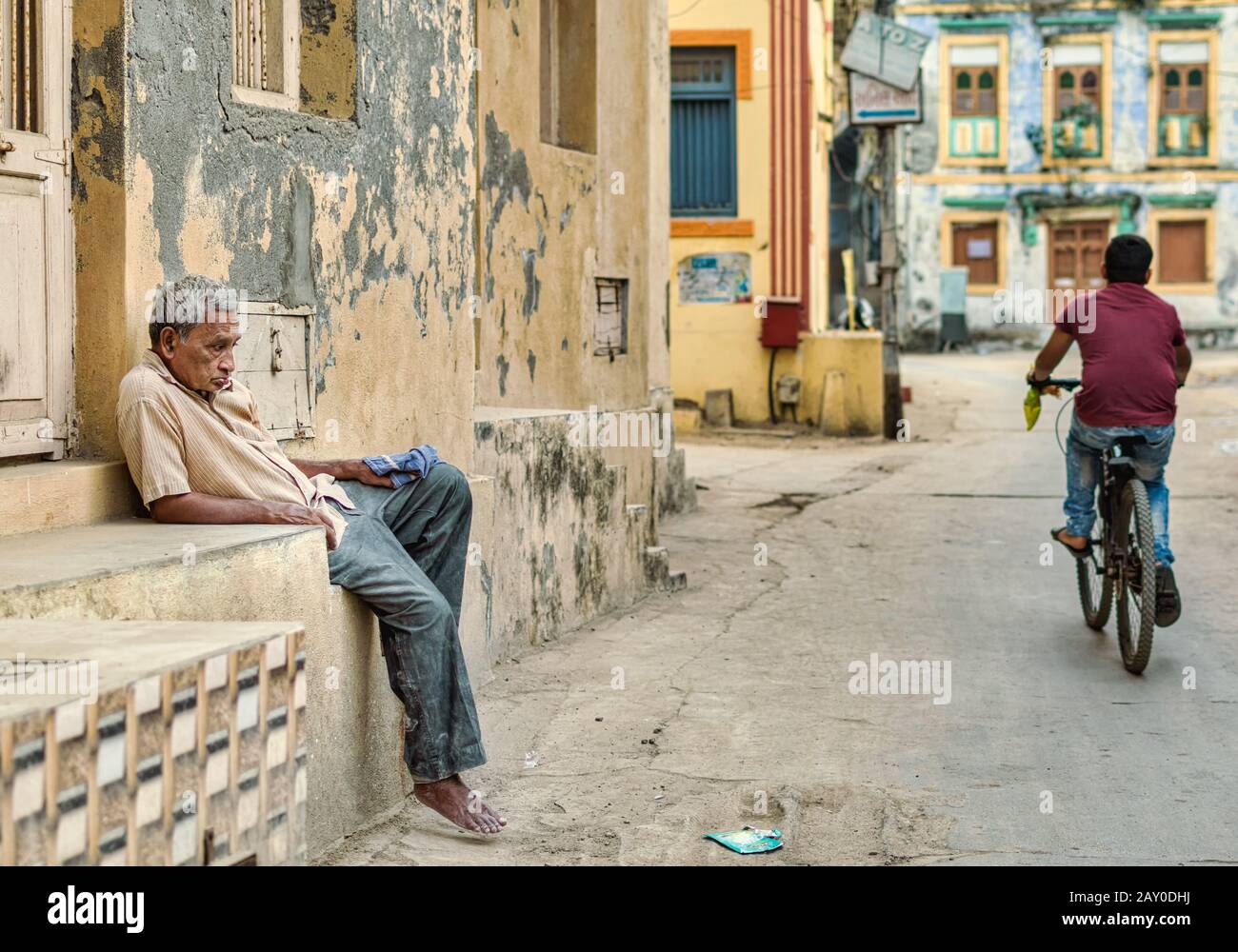 Diu, India - December 2018: An old man sits in a slumping posture outside a house on the quiet streets of the island of Diu. Stock Photo