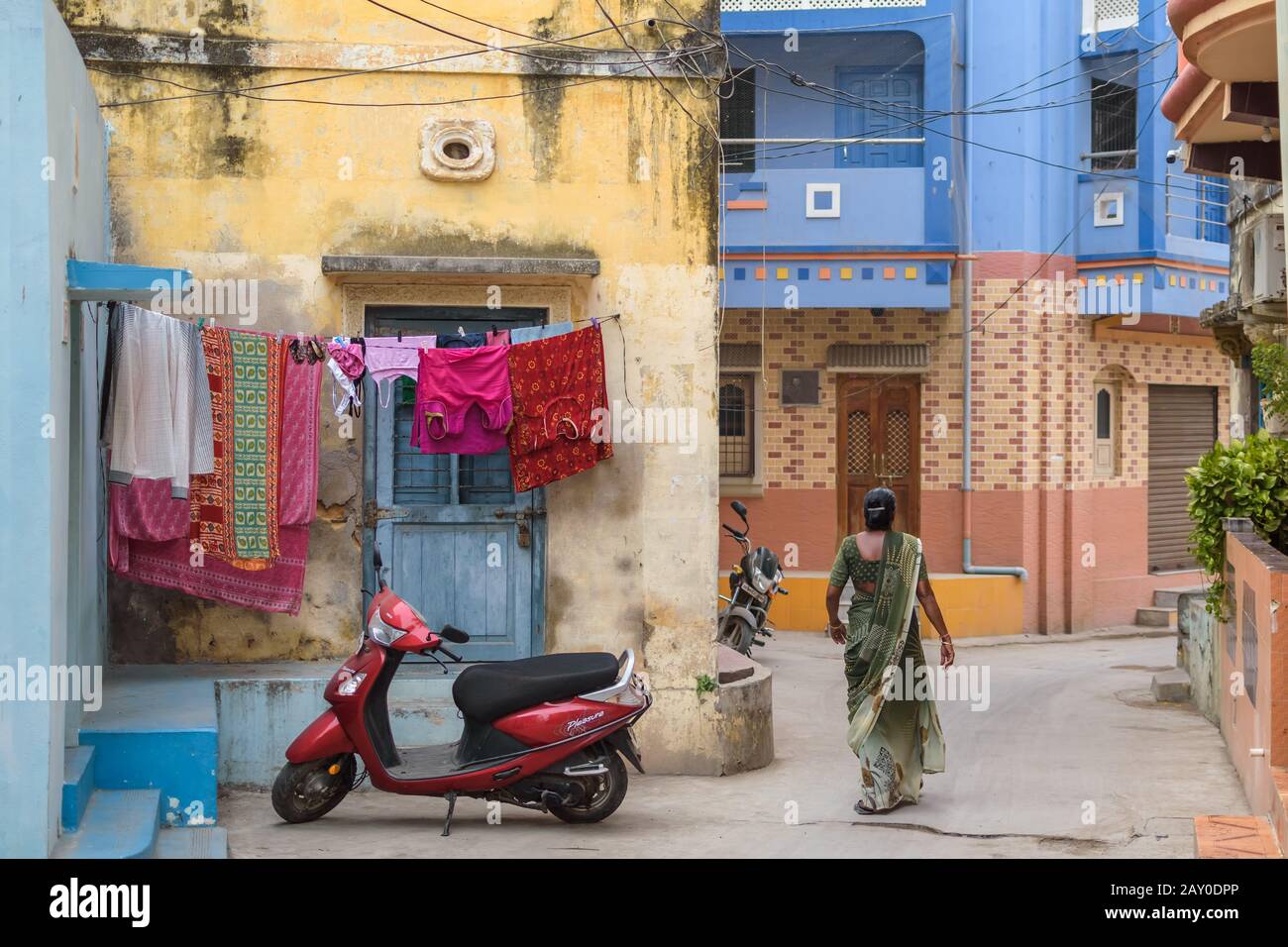 Diu, India - December 2018: Back profile of a woman who walks past a clothesline with drying clothes in the narrow lanes of a residential district in Stock Photo