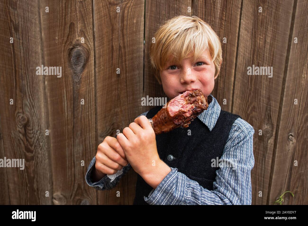 Boy standing by a fence eating a barbecued turkey leg, USA Stock Photo