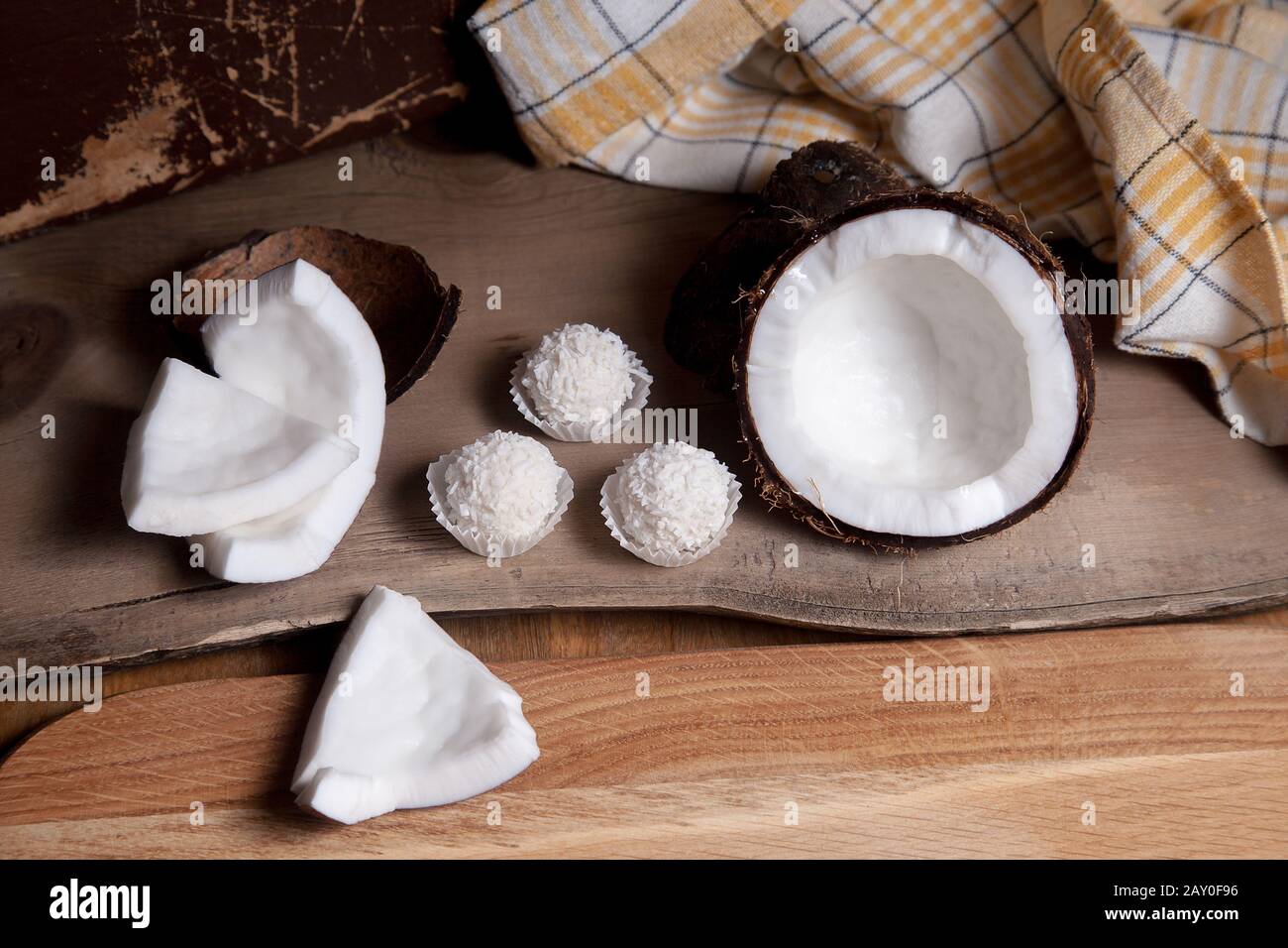 Coconut and sweet chocolate coconut truffles. Coconut shell, coconut flakes, small pieces of crashed nut and white chocolate coconut sweets on a woode Stock Photo