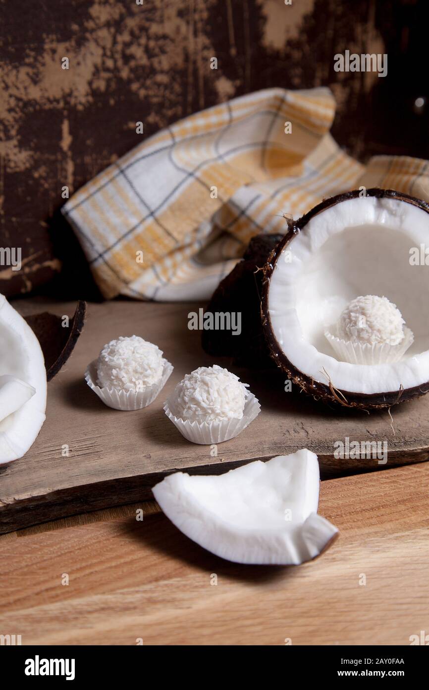 Coconut and sweet chocolate coconut truffles. Coconut shell, coconut flakes, small pieces of crashed nut and white chocolate coconut sweets on a woode Stock Photo