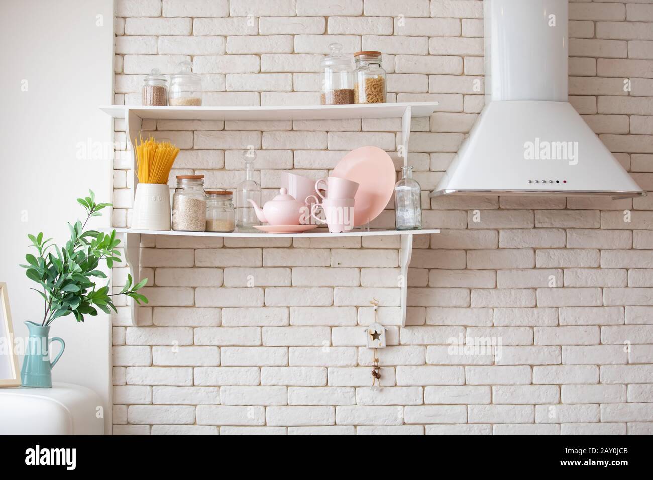 opened cupboard with white kitchenware inside. brick wall, shelves and