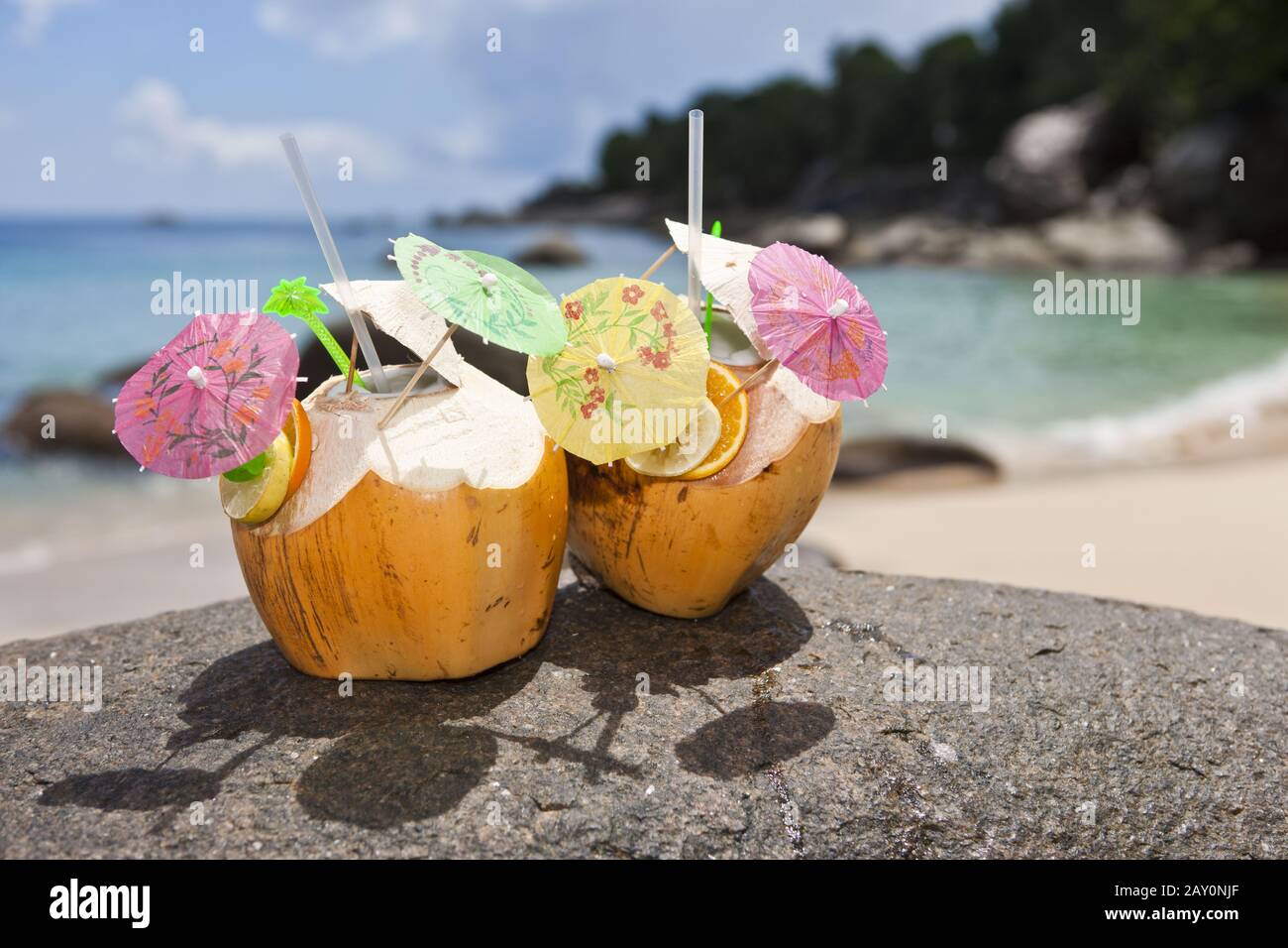 Two decorated coconuts filled with a drink stand on a granite rock Stock Photo