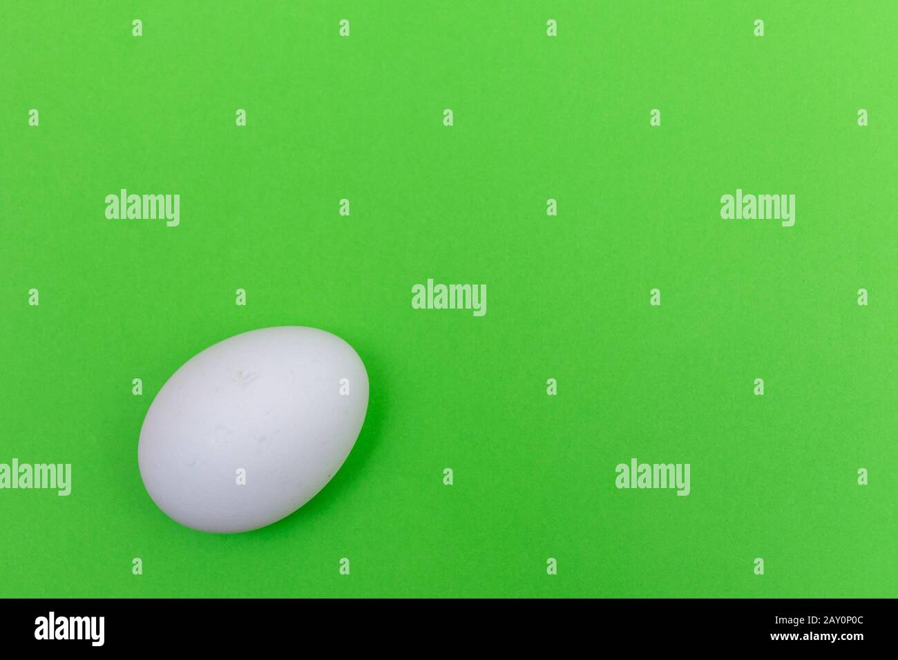 Easter holiday flat lay with white egg on a solid green background with copy space. Stock Photo