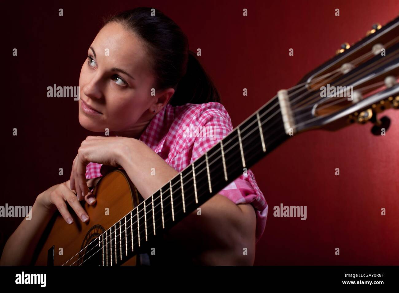 Woman holding classical guitar against a red background Stock Photo - Alamy
