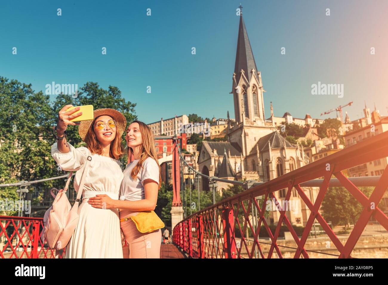 Two happy girls friends walking on Saint Georges pedestrian bridge while traveling in Lyon old town in France Stock Photo