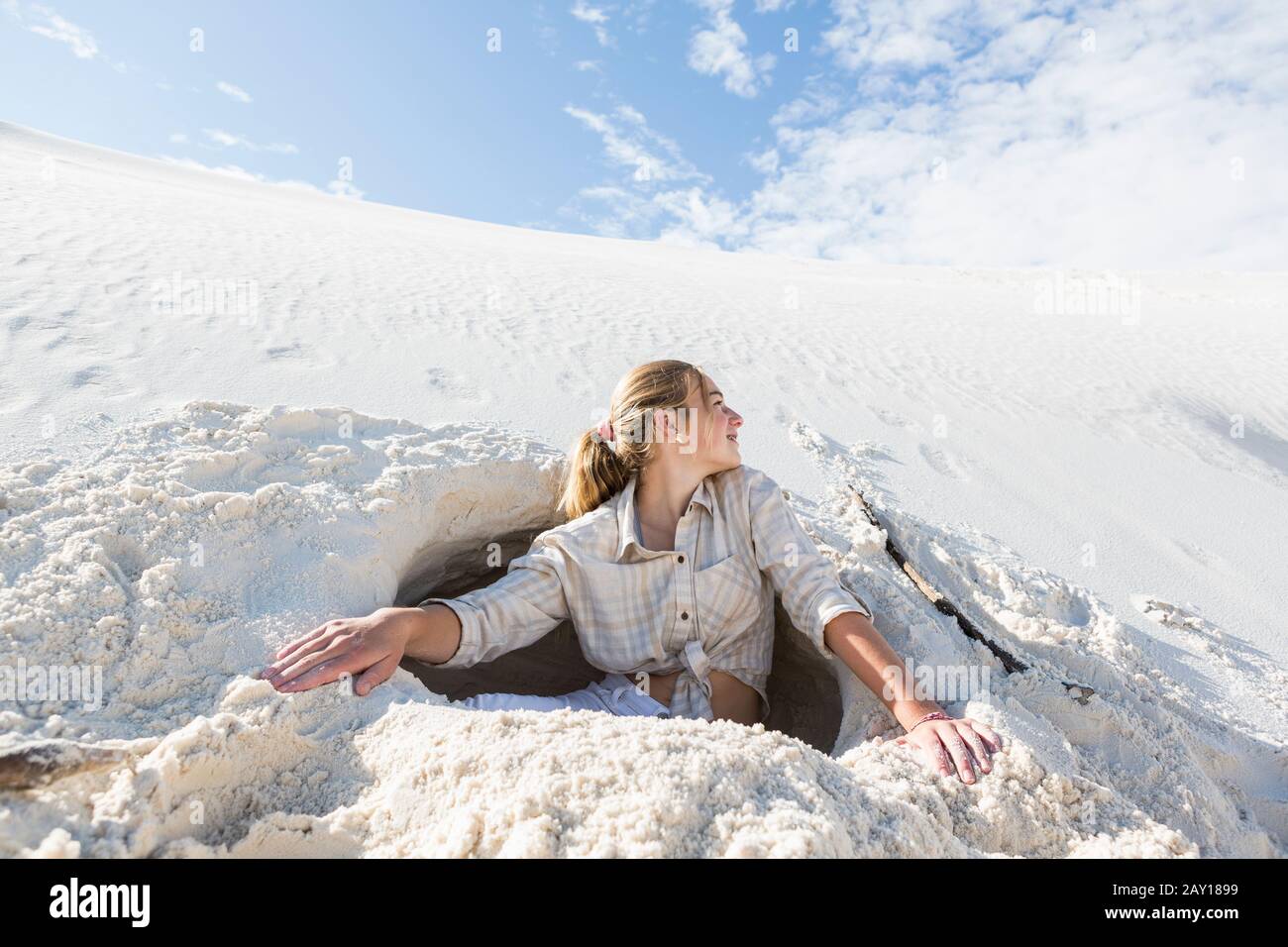 13 year old girl emerging from a dug out hole in white sand dunes Stock  Photo - Alamy
