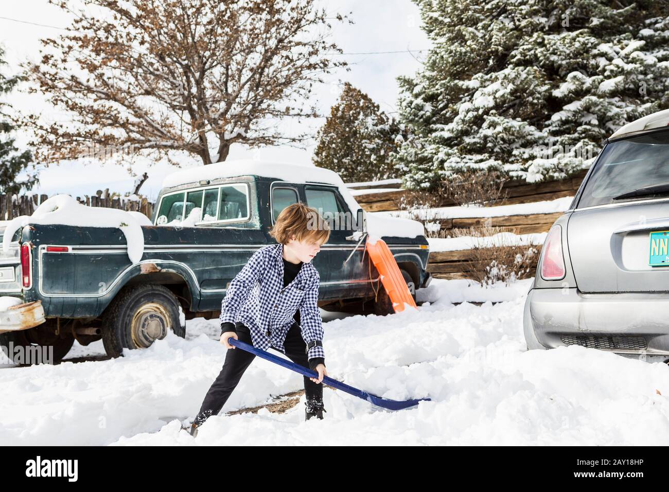 A six year old boy shoveling snow in driveway Stock Photo