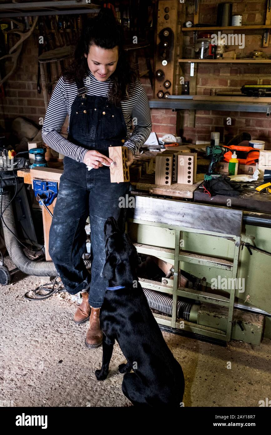 Woman with long brown hair wearing dungarees standing in wood workshop ...