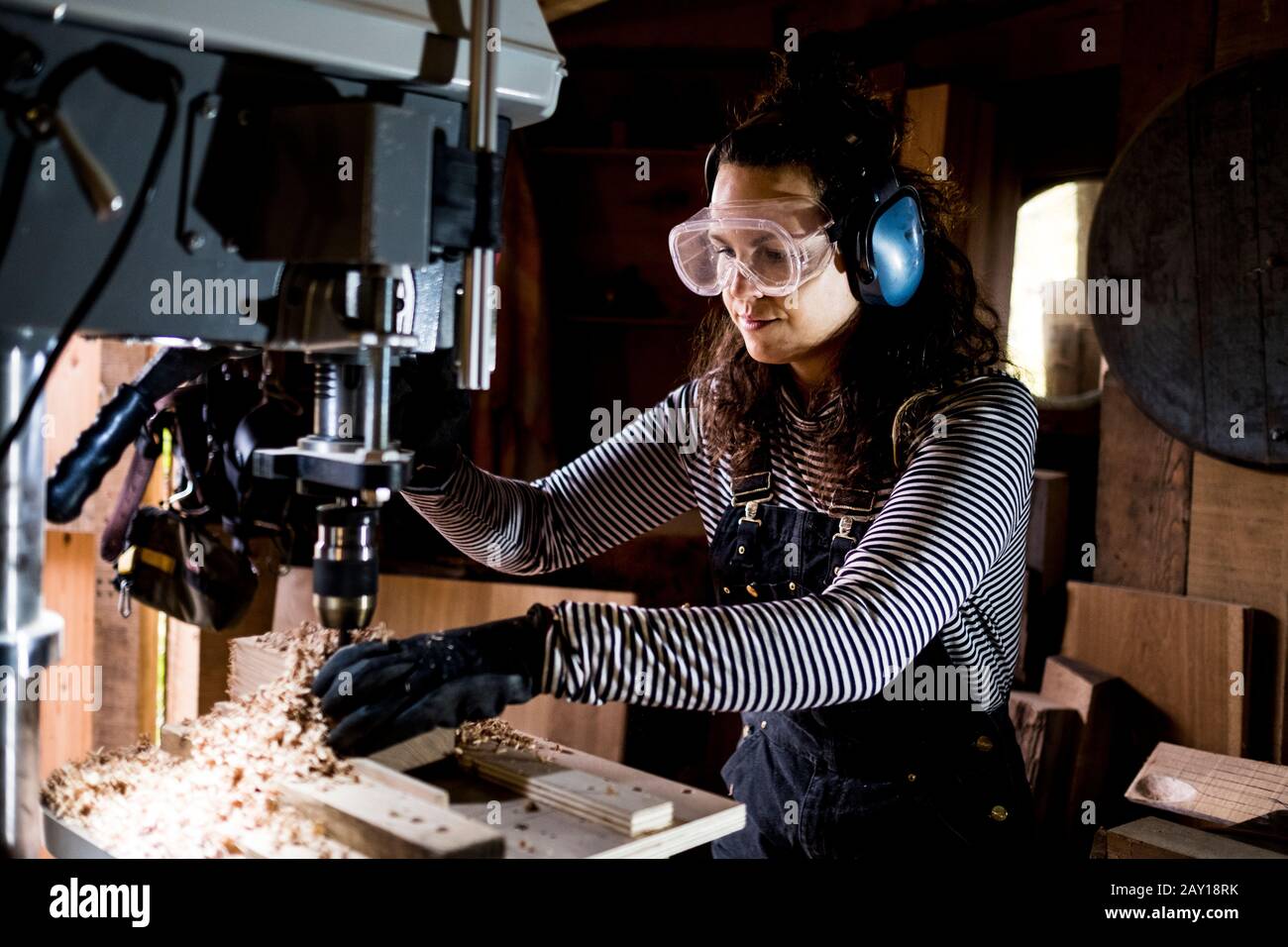 Woman with long brown hair wearing dungarees, safety glasses and ear ...