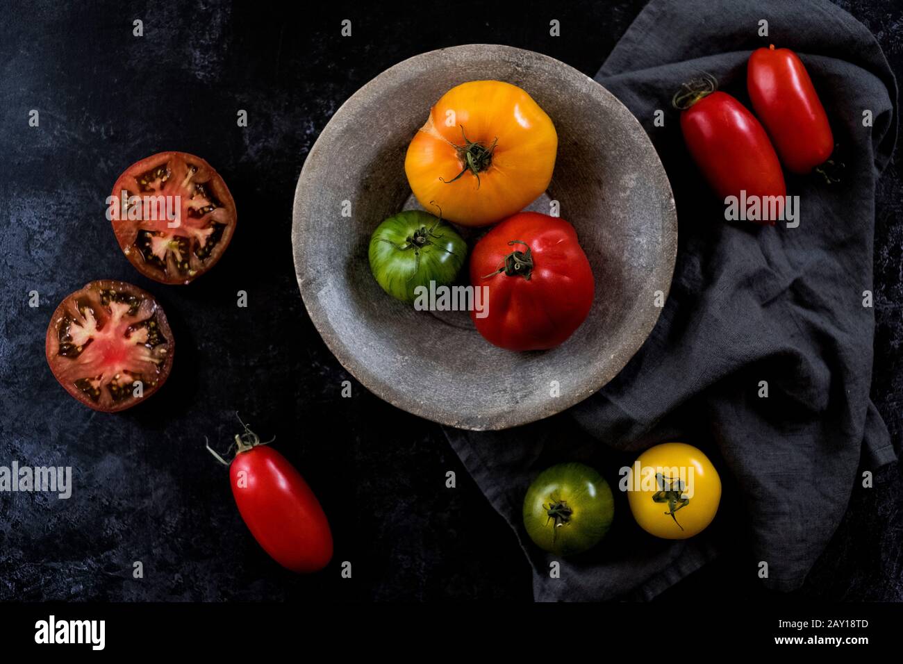 High angle close up of grey plate and cloth and a selection of fresh tomatoes on black background. Stock Photo