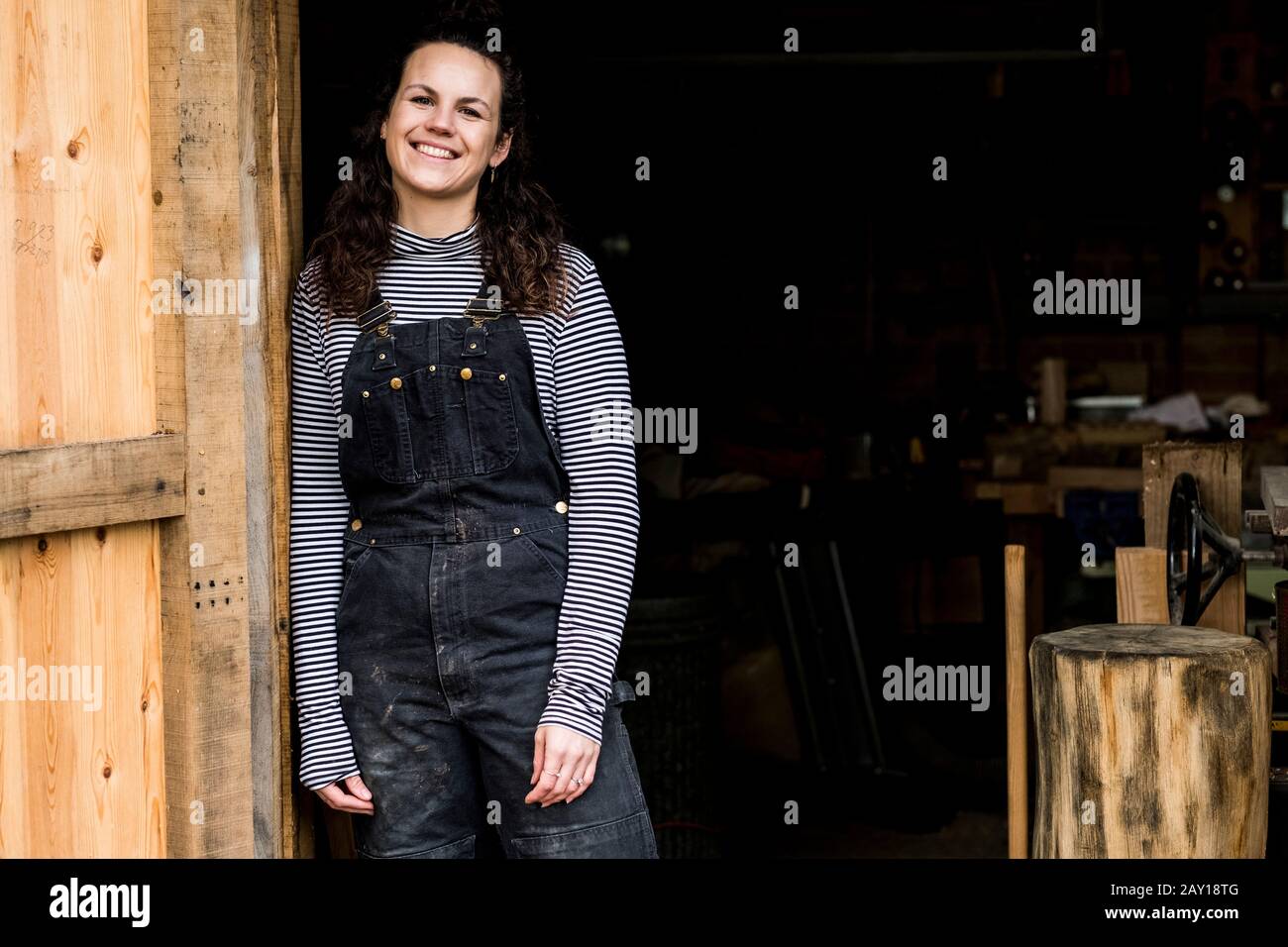 Woman with long brown hair wearing dungarees standing at entrance to ...